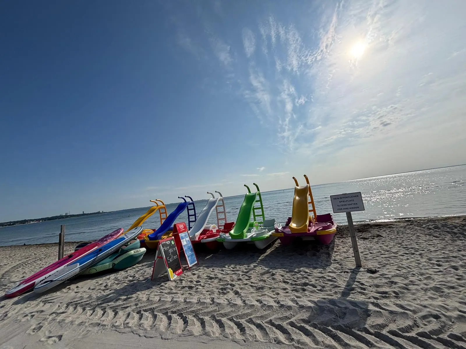 Tretboote mit bunten Rutschen am Wasser, daneben Stand-up-Paddle-Boards